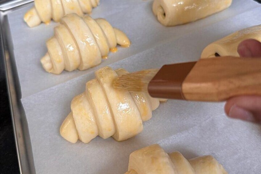 A person applying glaze to pastries on a baking sheet. 1