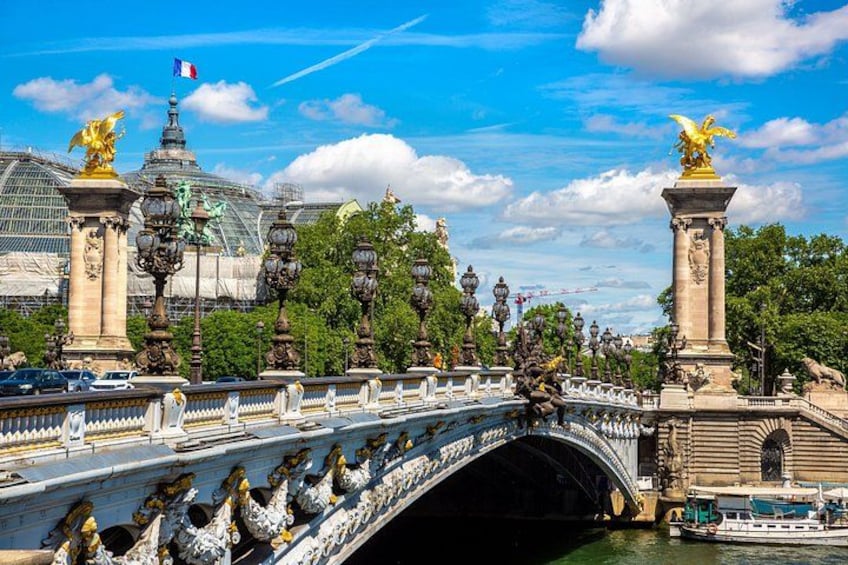 A bridge with ornate statues, a river, and a building with a glass facade in the background. 3