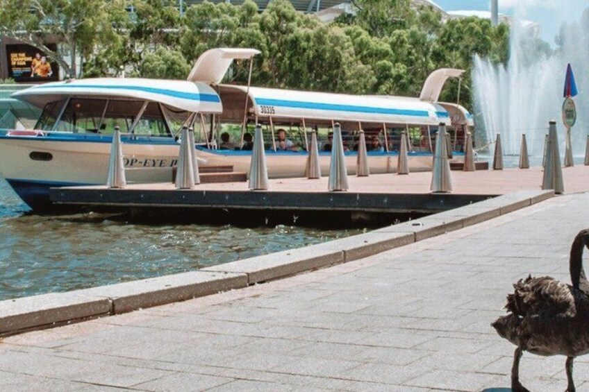 A boat with 'OP-EYE' written on it docked at a waterfront promenade with a fountain in the background. 2