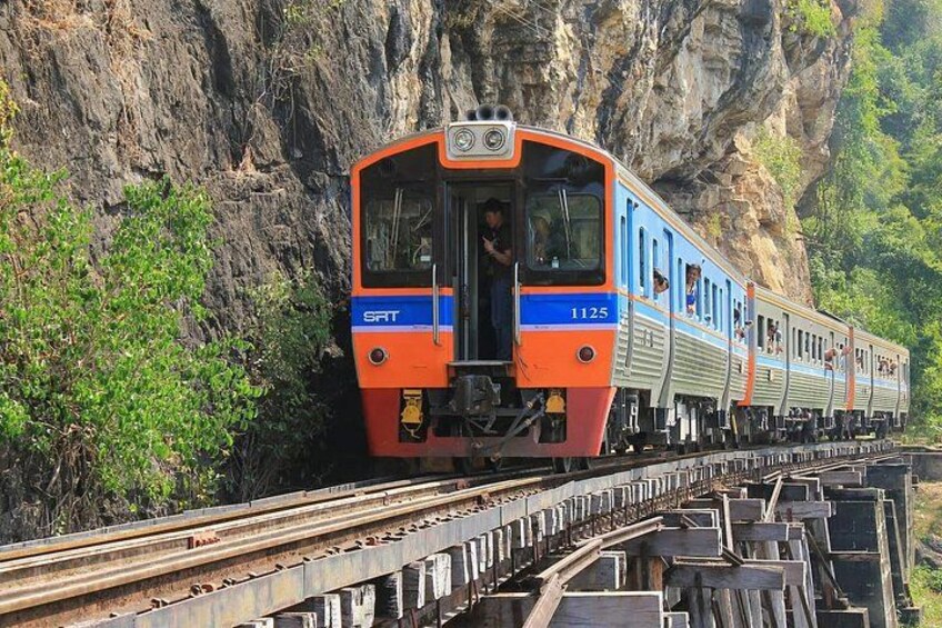 A train with the number 1125 traveling on tracks surrounded by rocky cliffs and greenery. 1