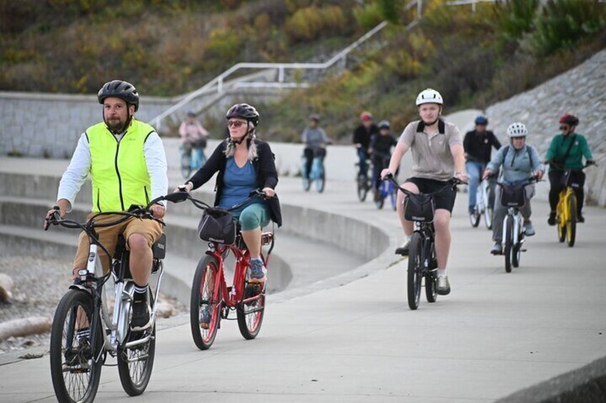 Cyclists on a paved path with a concrete barrier and steps in the background. 3