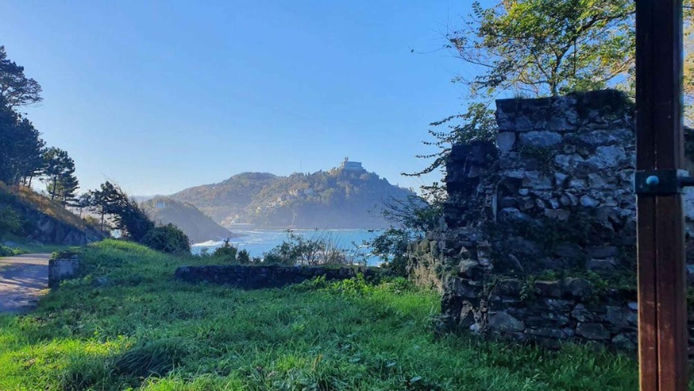 A coastal landscape with a stone wall, greenery, and a hill with a building on top. 3