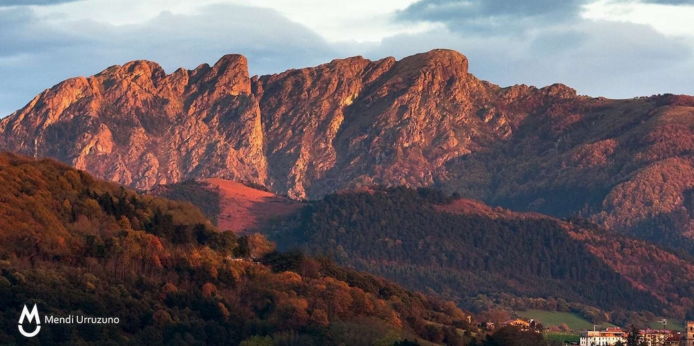 A rugged mountain range with autumn foliage, a valley, and a small settlement in the foreground. 2