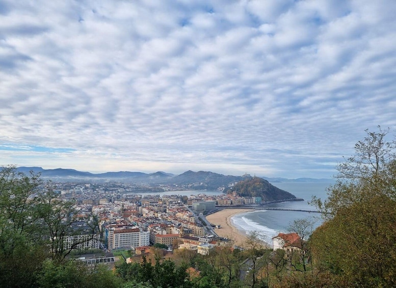 A coastal cityscape with a beach, mountains, and a cloudy sky. 5