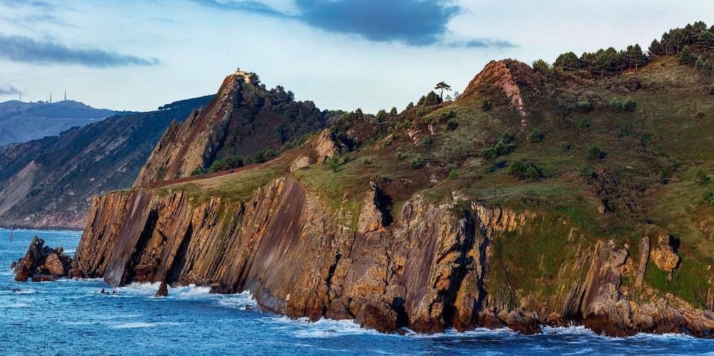 A coastal cliff with a lighthouse on top, rugged terrain, and the ocean. 1