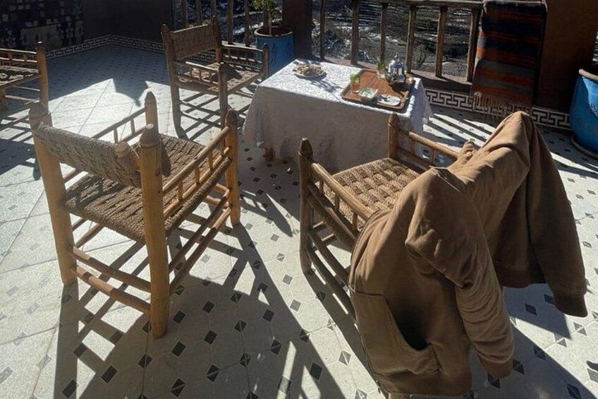 Outdoor seating with woven chairs and a table, a blue container, and a patterned floor. 4