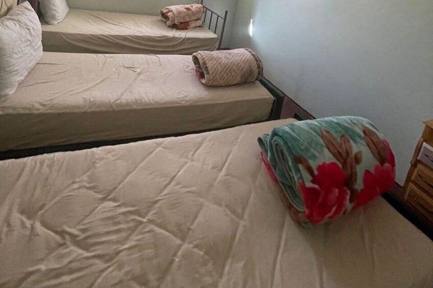A dormitory room with two beds, each with a beige mattress and pillows. 2