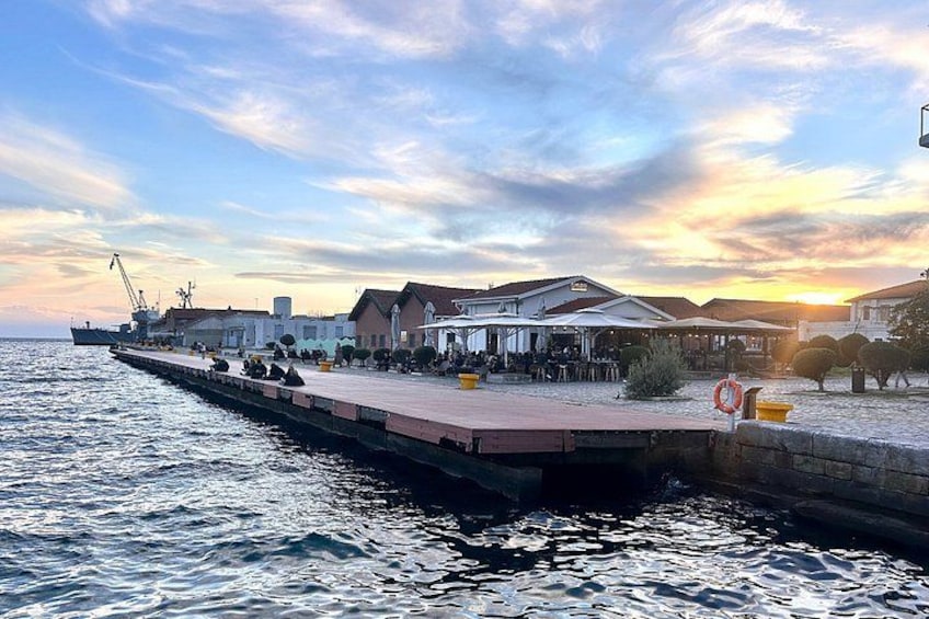 A waterfront promenade with a pier extending into the water, buildings, and a sunset in the background. 4