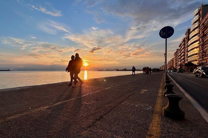A sunset over a waterfront promenade with people walking, a building on the right, and a clear sky. 2