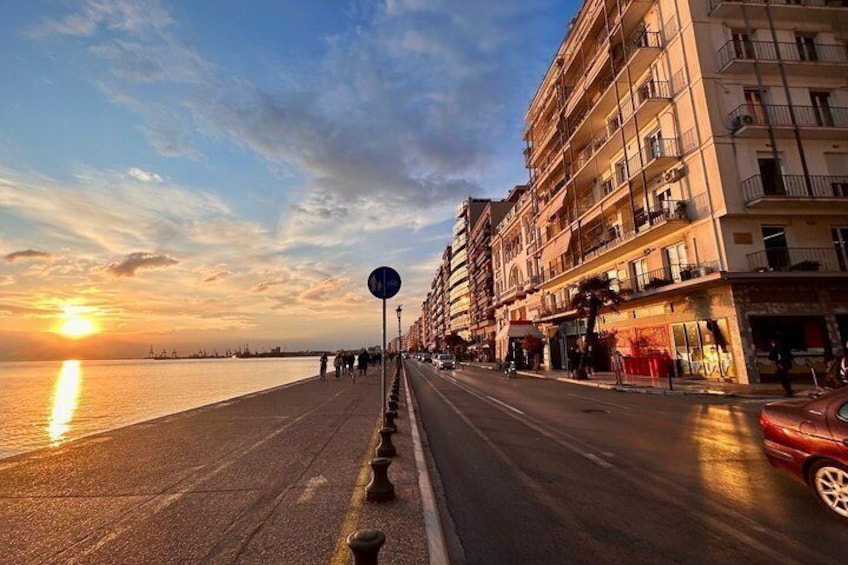 A waterfront promenade with buildings, a sunset, and a red car. 3