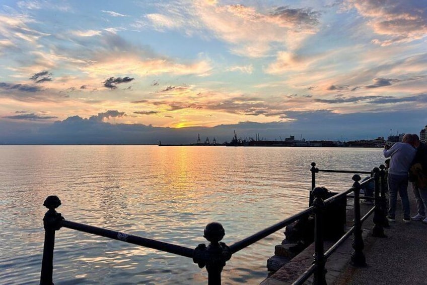 A sunset over a calm body of water with a railing and people standing on the shore. 5