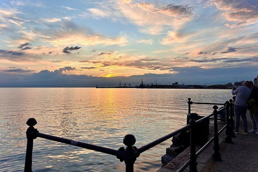 A sunset over a calm body of water with a railing and people on a pier. 5