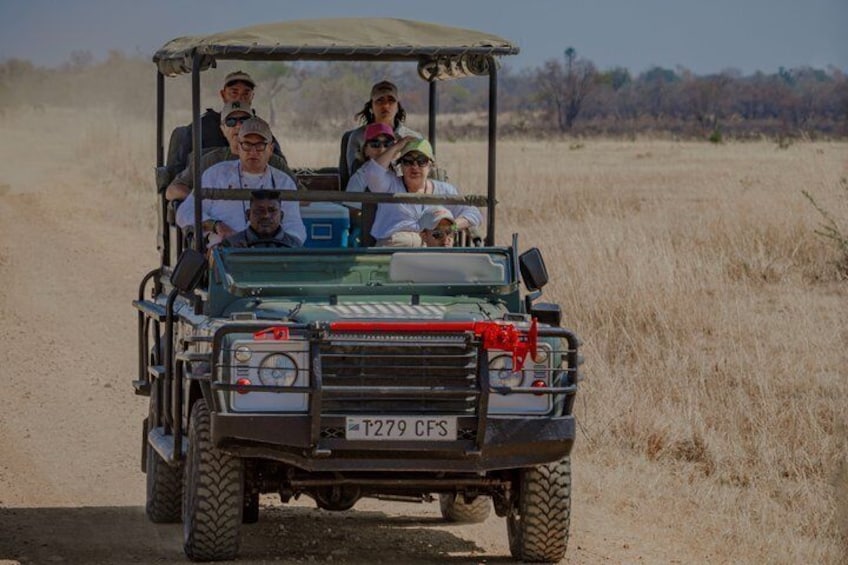 A safari vehicle with passengers, traversing a dry grassland. 1