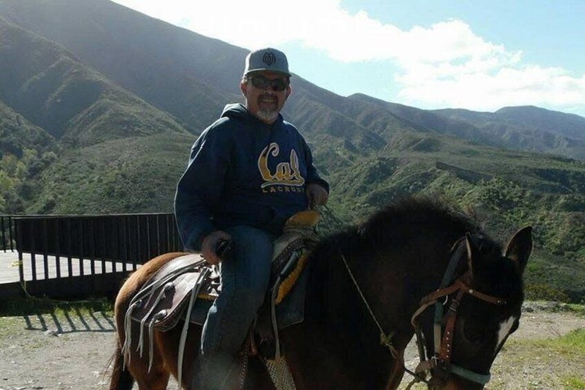 A person riding a horse on a dirt path with mountains in the background. 2