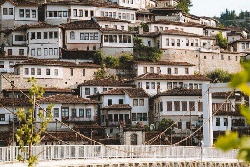 A hillside of white buildings with red-tiled roofs, a bridge in the foreground, and greenery in the foreground. 3