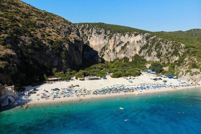 A coastal beach with clear turquoise waters, a rocky cliff, and beach umbrellas. 4