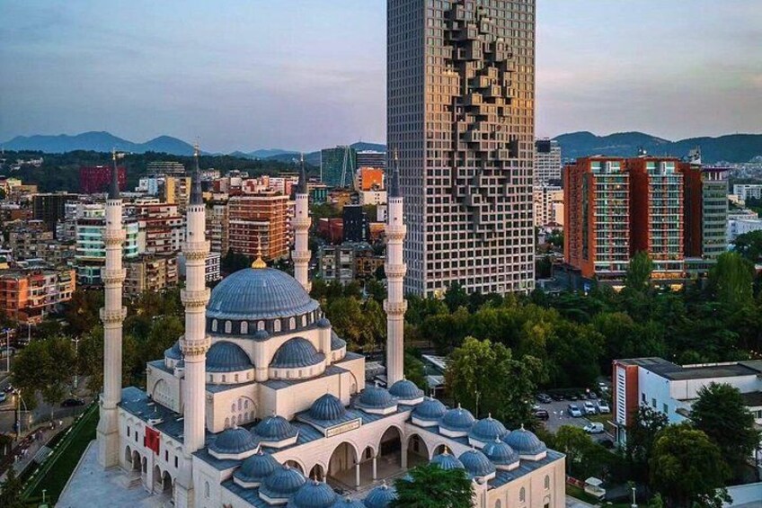 A mosque with multiple domes and minarets, surrounded by modern buildings and a mountainous backdrop. 1