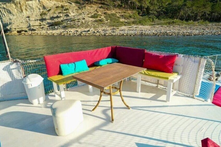 A boat deck with a wooden table, colorful cushions, and a white bench. 2