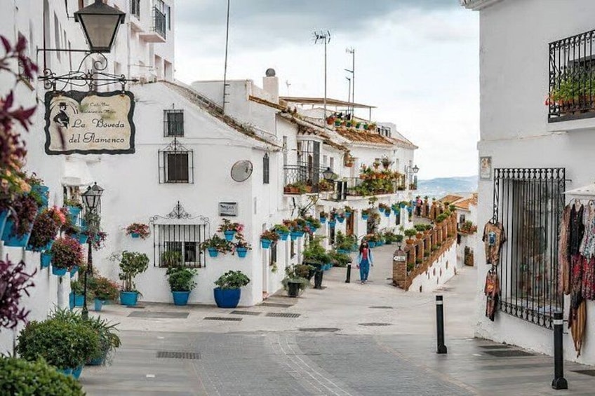 A narrow street lined with white buildings, potted plants, and hanging laundry. 2