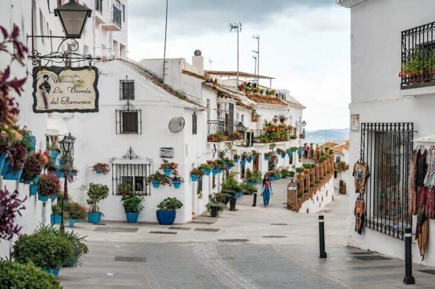 A narrow street lined with white buildings, potted plants, and hanging laundry. 3