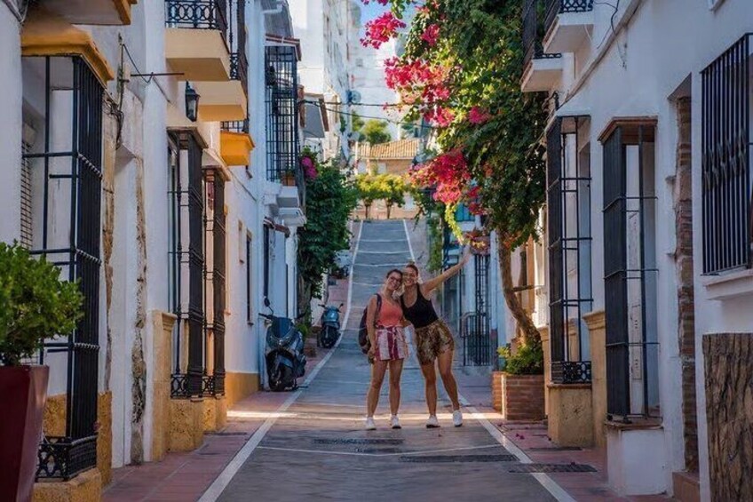 A narrow street with white buildings, balconies, and a scooter parked on the side. 4