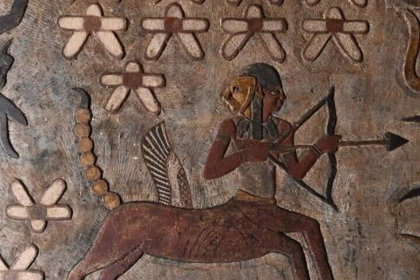 An ancient Egyptian mural with a figure of a person with a bow and arrow, a falcon, and a seated dog. 1