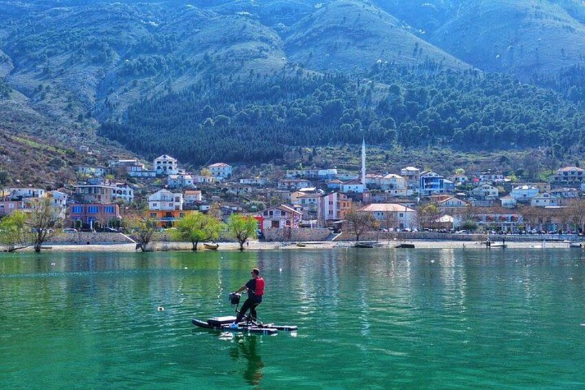 A person on a paddleboard in a lake with houses and mountains in the background. 1