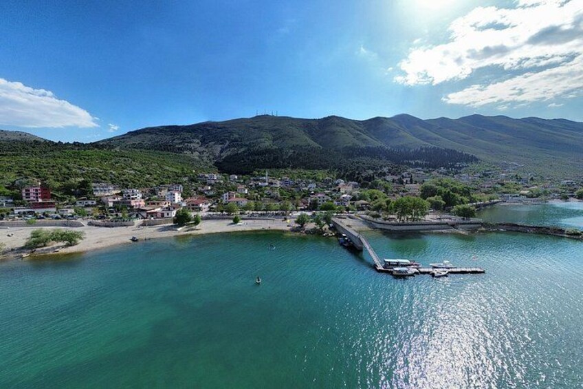 A coastal town with a dock, clear blue water, and mountains in the background. 3