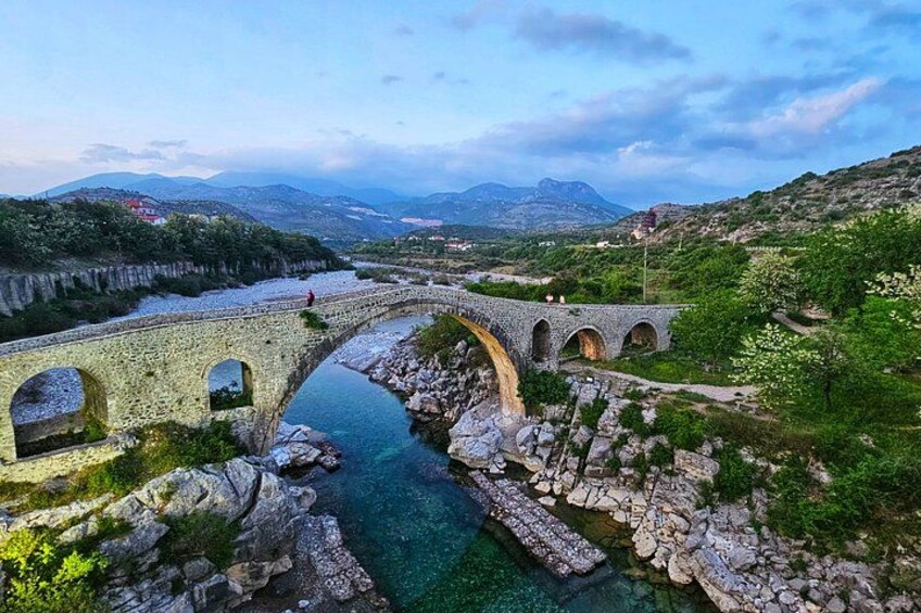 A stone bridge over a river, surrounded by greenery and mountains. 4