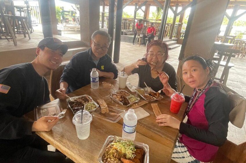 Four people dining at an outdoor wooden table with various dishes and drinks. 2