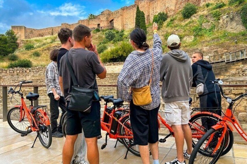 A group of people observing a historical site with bicycles parked nearby. 2