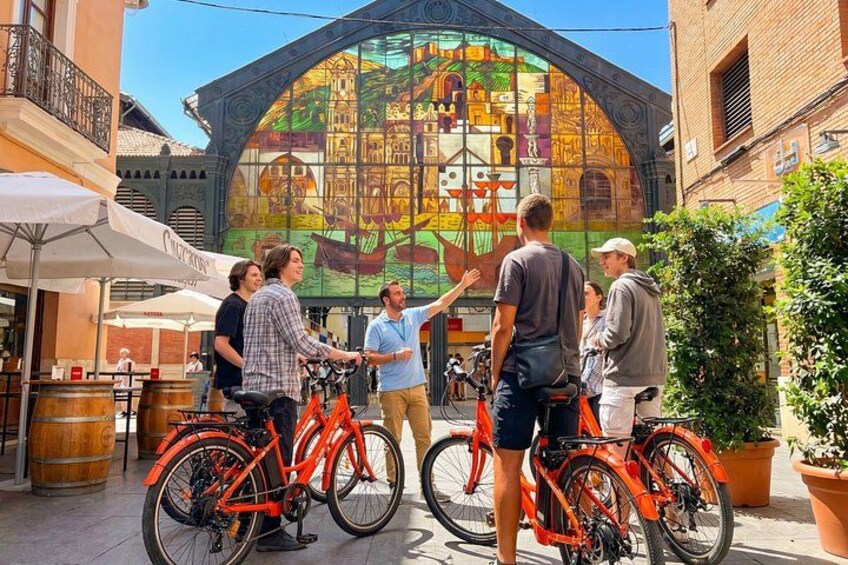 A group of people standing around bicycles in front of a colorful stained glass window. 1