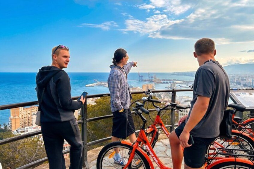 Tres personas en un balcón con vista a una ciudad y al mar. 4