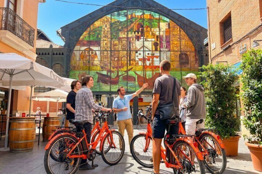 A group of people standing in front of a colorful stained glass window, with bicycles parked in the foreground. 1