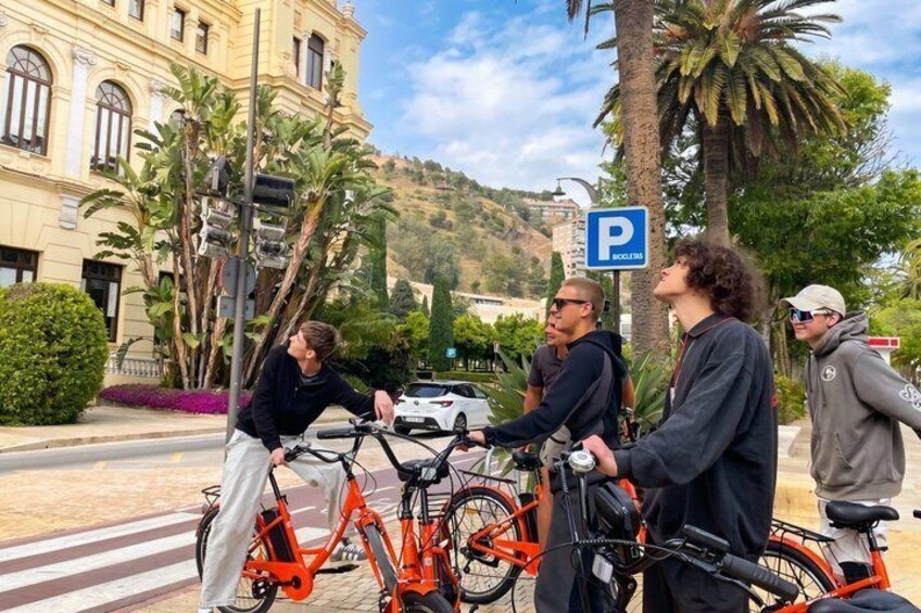 Four people standing on a crosswalk with bicycles, a parking sign, and a building in the background. 3