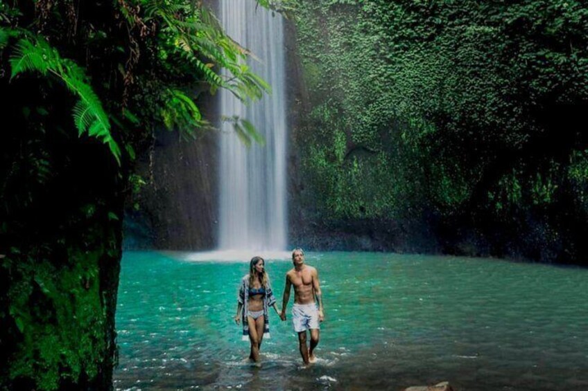 Two people walking in a forested area with a waterfall. 1