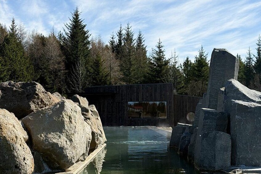 A wooden structure near a body of water with large rocks and trees in the background. 3