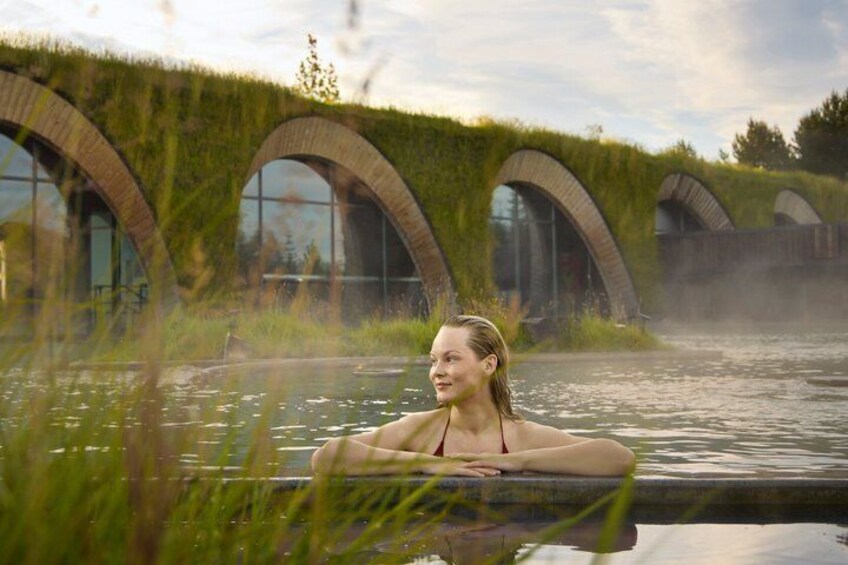 A person in a hot tub with a natural, green roofed structure in the background. 1