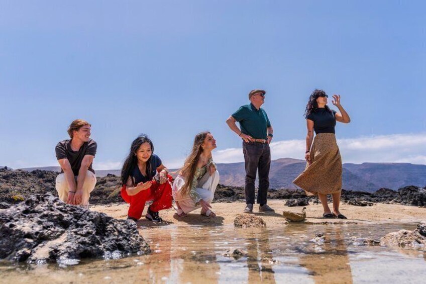 A group of people on a rocky beach with water and mountains in the background. 4