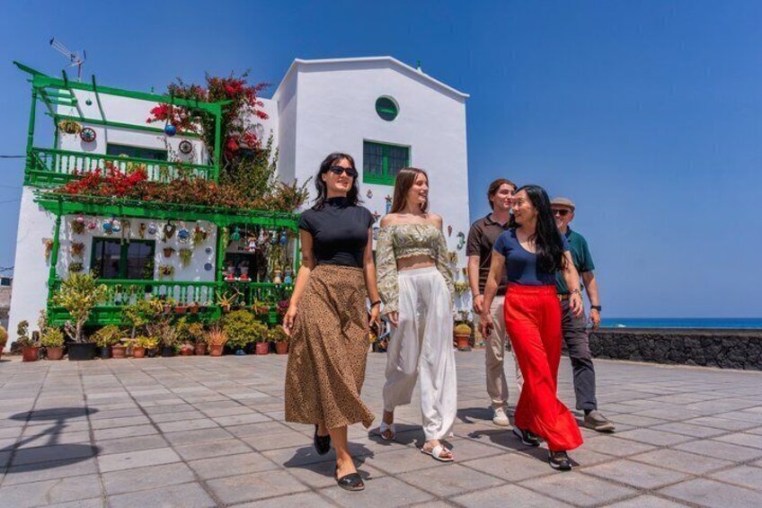 A group of people walking on a paved area with a white building and green balcony with plants in the background. 5