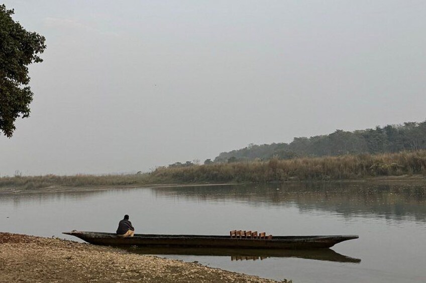 A person sitting on a boat on a calm body of water with a forested shoreline in the background. 1