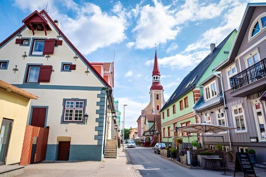 A street lined with colorful buildings, a church with a red spire, and a clear blue sky. 5