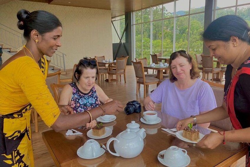 A group of people sitting at a table with teapots and cups, engaged in conversation. 3