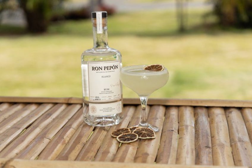 A bottle of Ron Pepeón Blanco rum and a martini glass with a dried orange slice on a wooden table. 1