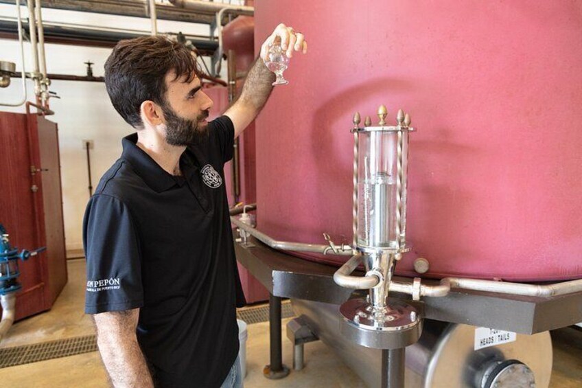 A person in a black shirt with a logo, standing next to a large red tank and a cylindrical glass apparatus. 3