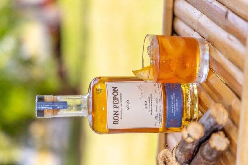 A bottle of Ron Pepeón with a label, placed on a wooden surface with a blurred natural background. 4