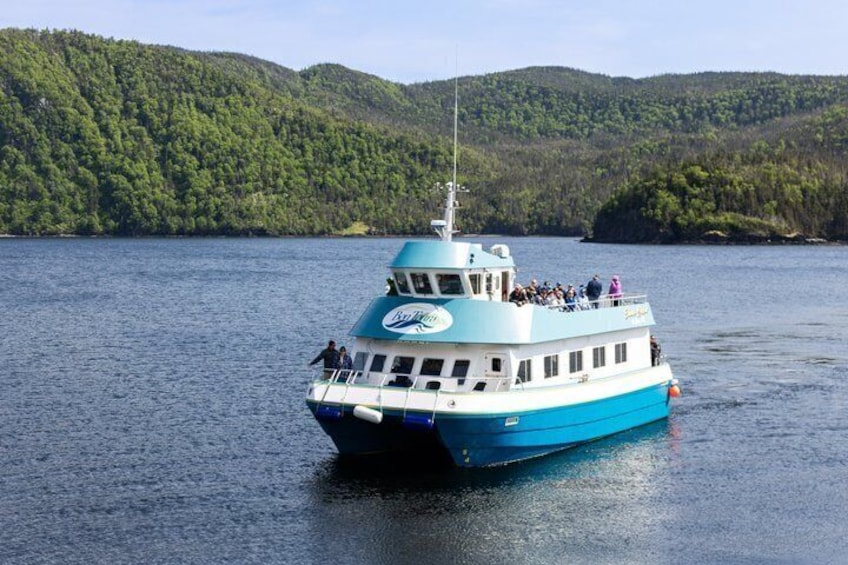 A blue and white boat with passengers on a calm lake surrounded by forested hills. 2