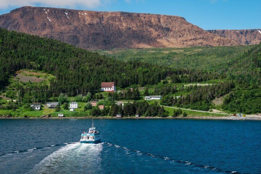 A boat on a lake with houses and a mountain in the background. 1
