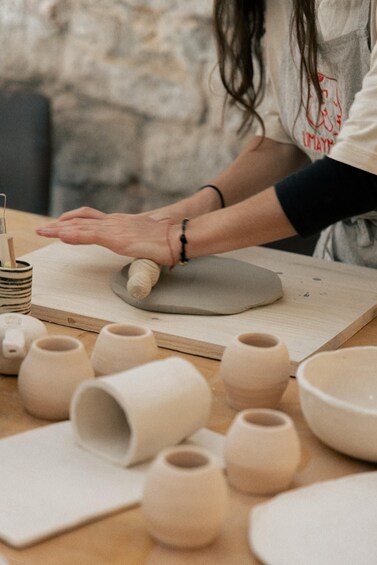 A person shaping clay on a wooden board, surrounded by various pottery items. 1