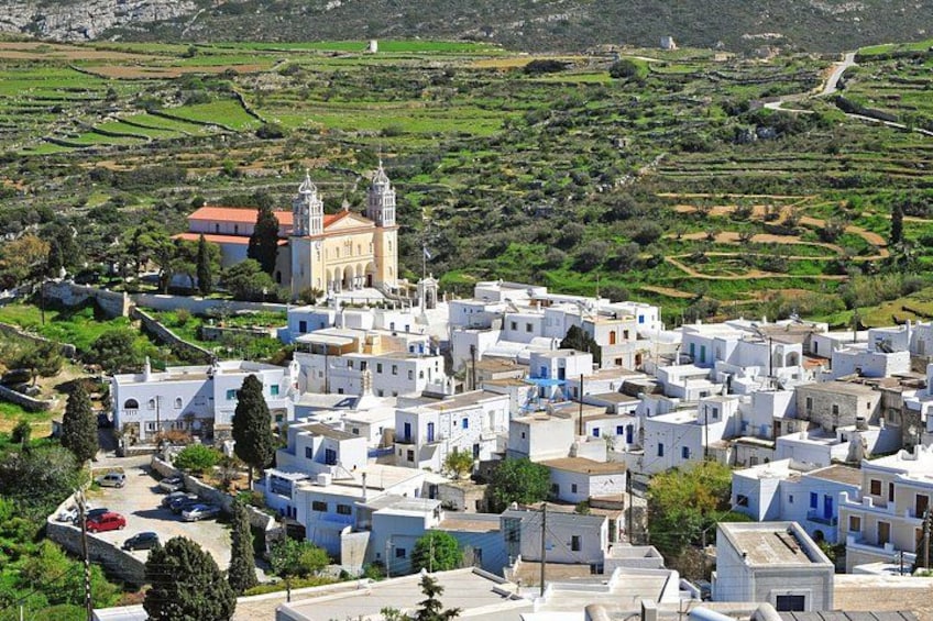 A coastal village with white buildings, a church with two towers, and terraced fields in the background. 1